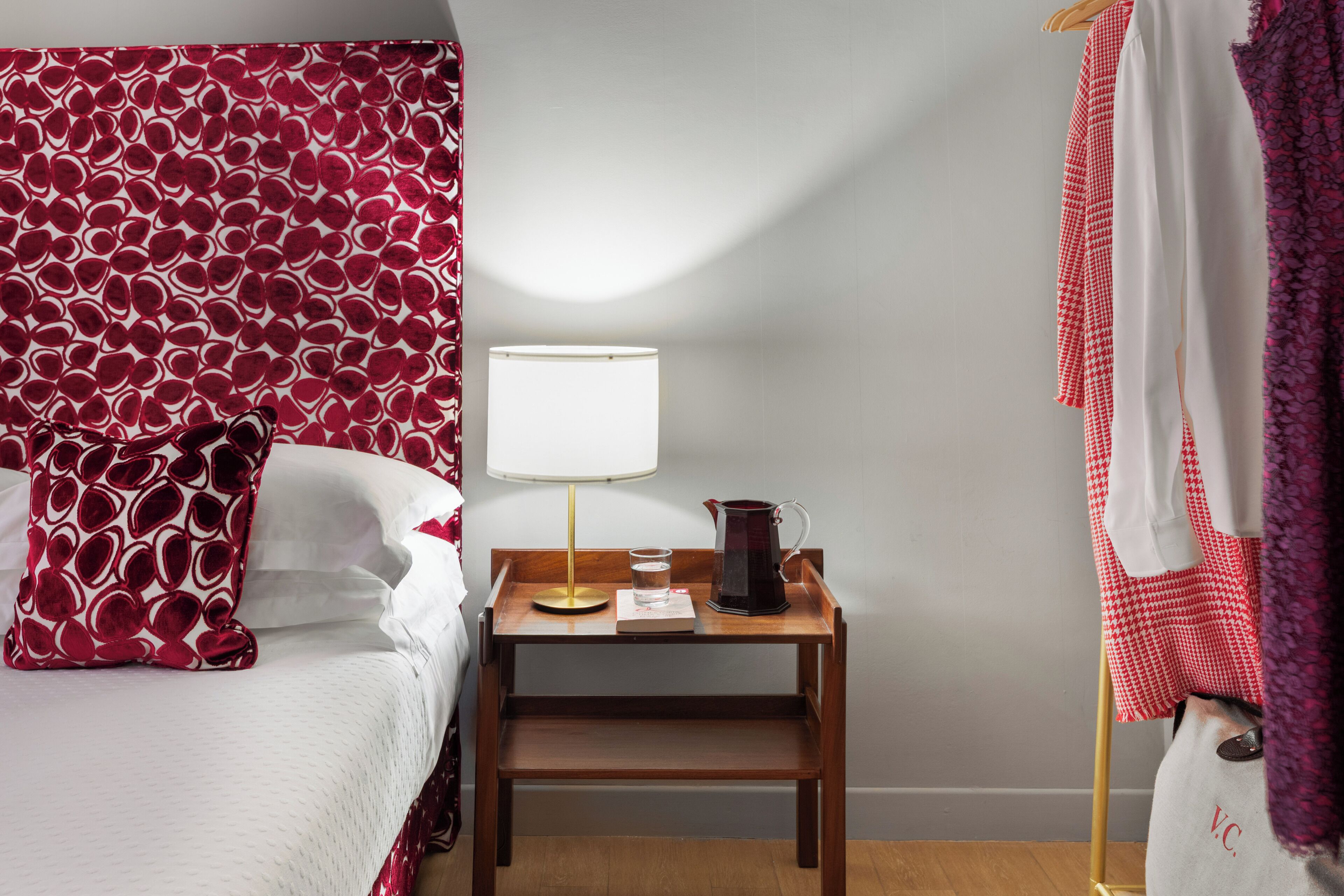 A hotel room with a bed, a bedside table with a lamp, a kettle, and a glass of water.