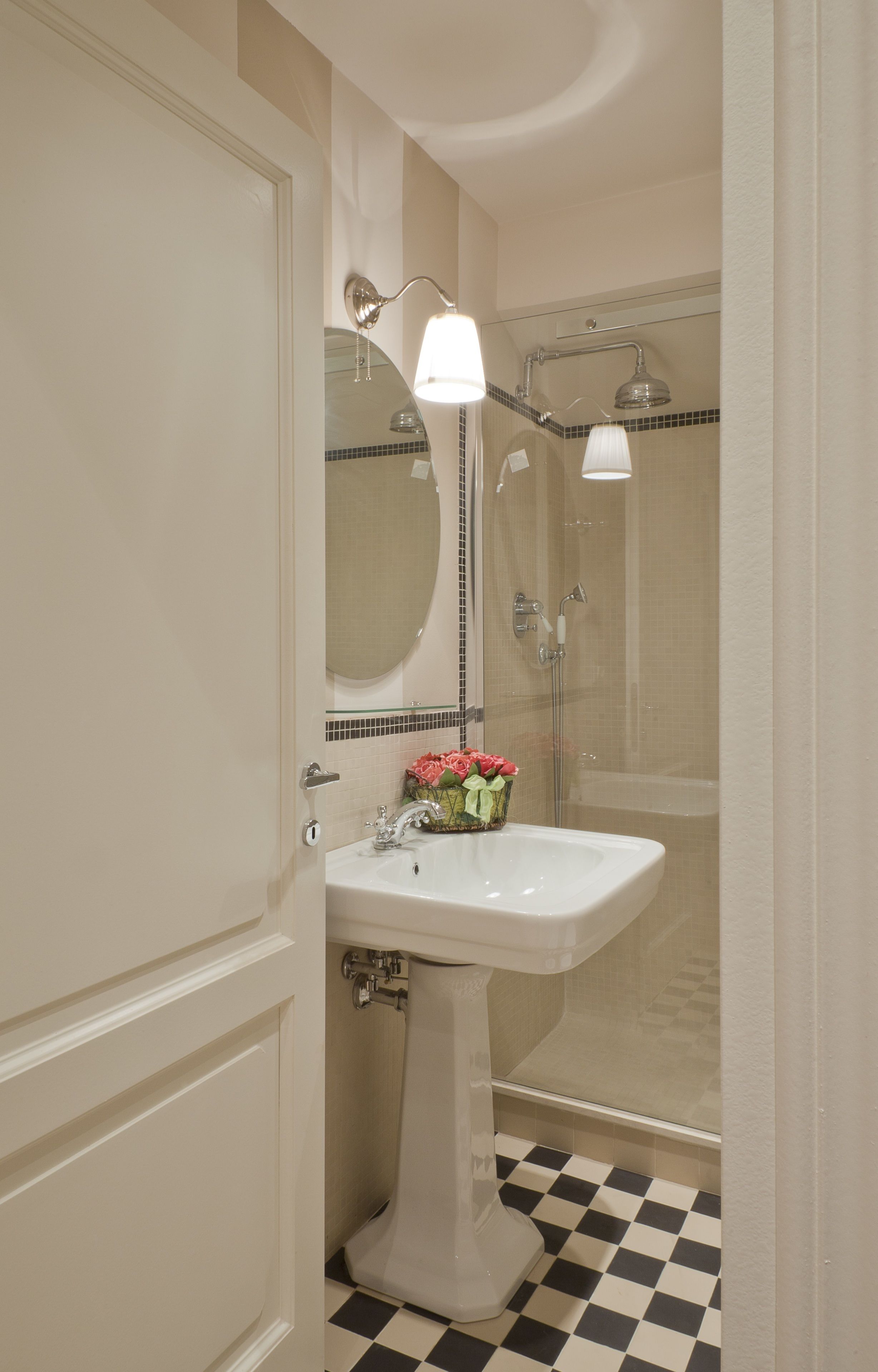 A bathroom with a white pedestal sink, a mirror, a shower, and a checkered floor.