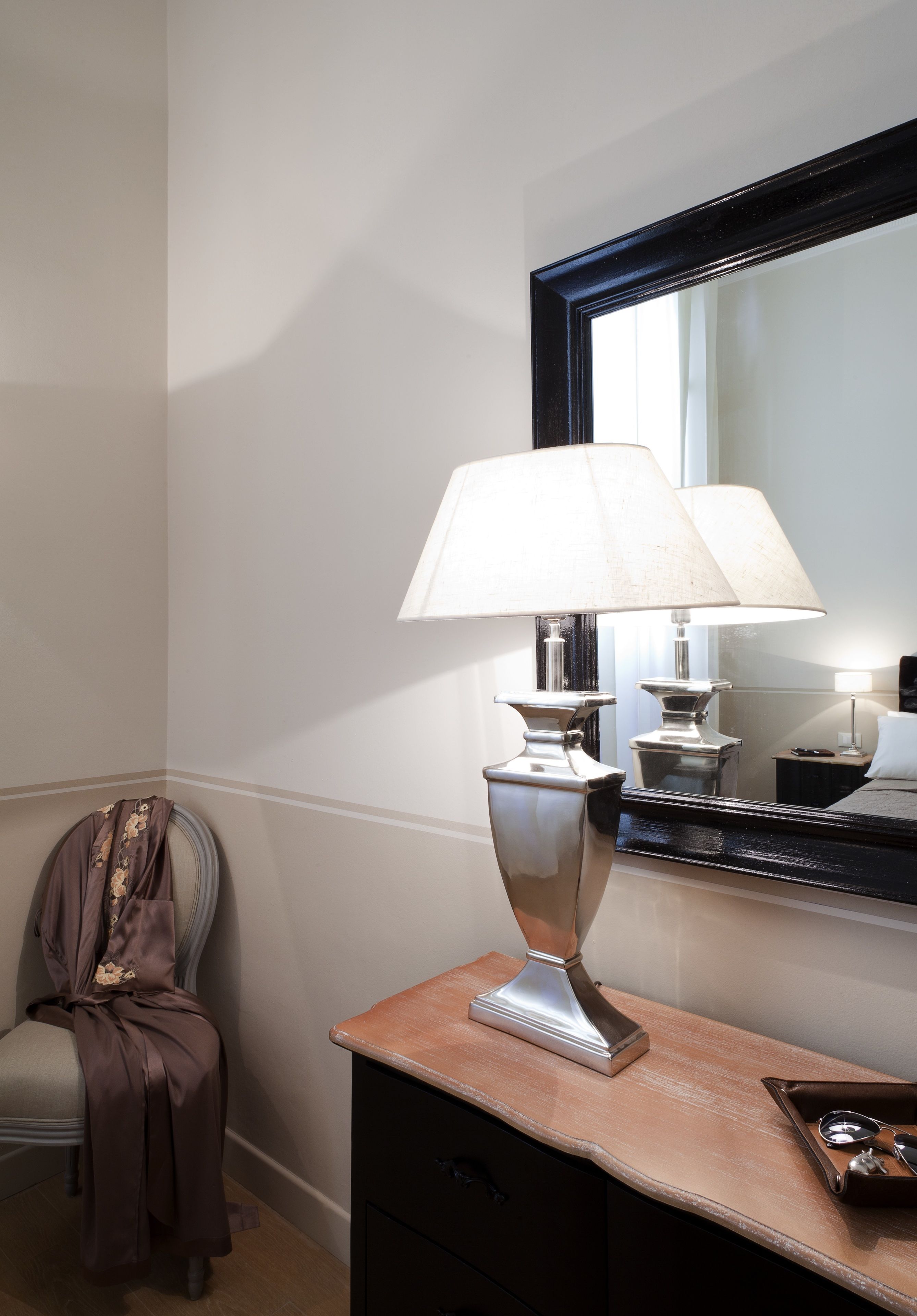 A room with a large mirror, a lamp, a chair, and a small table with a tray.