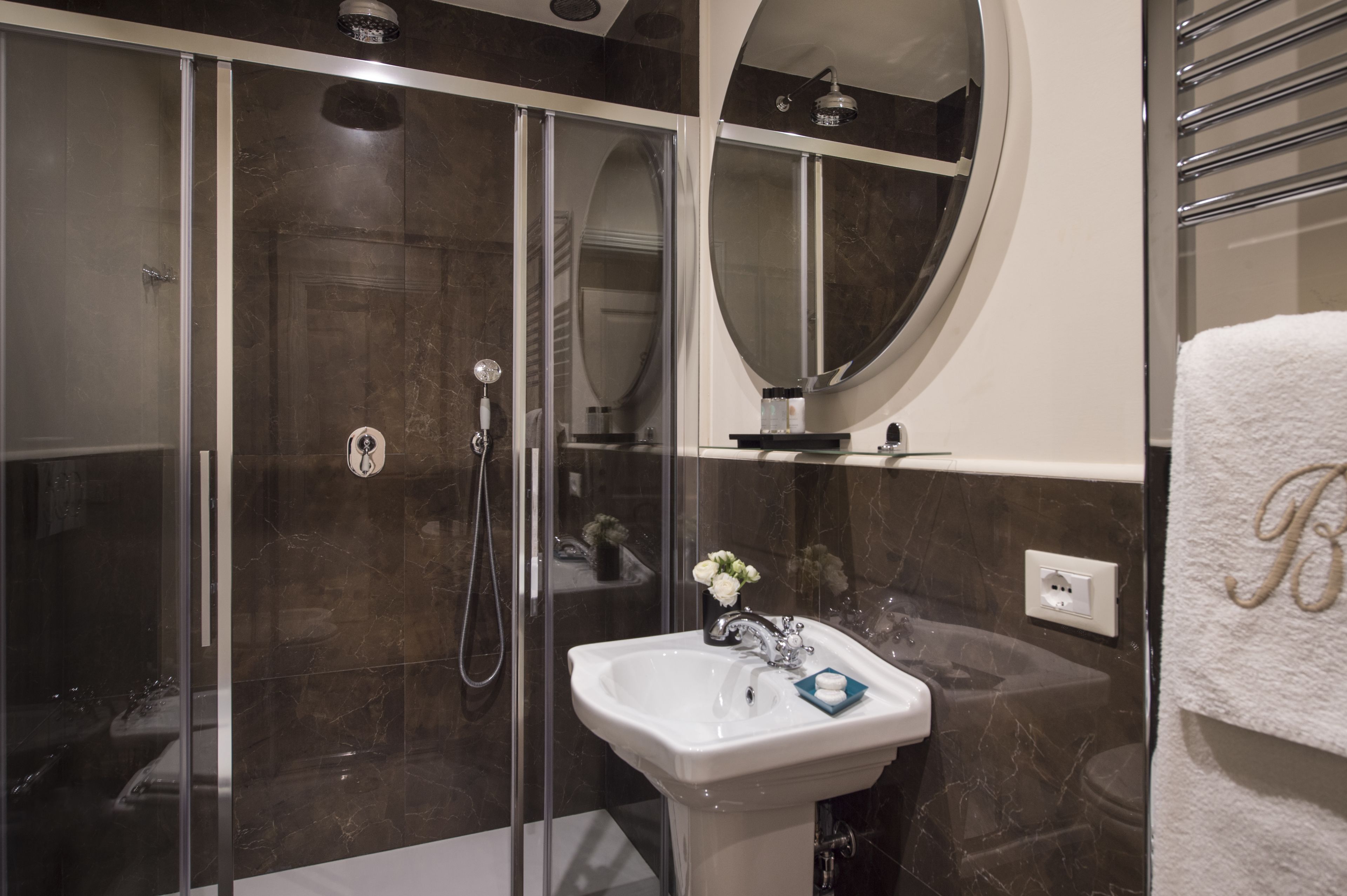 A modern bathroom with a glass-enclosed shower, a white sink with a vase of flowers, and a towel rack with a towel.