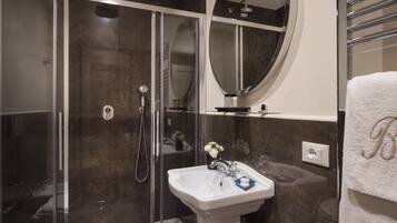 A modern bathroom with a glass-enclosed shower, a white sink with a vase of flowers, and a towel rack with a towel.