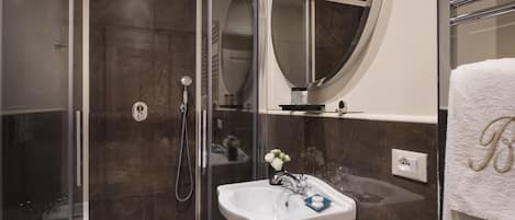 Ein modernes Badezimmer mit einer gläsernen Duschkabine, einem weißen Waschbecken mit Blumen in einer Vase und einem Handtuchhalter mit einem Handtuch.