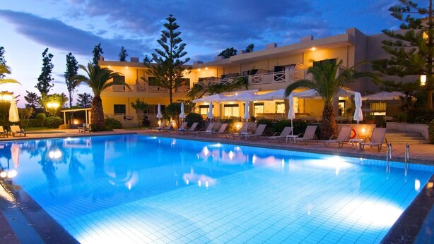 A swimming pool with lounge chairs and umbrellas, surrounded by a building with multiple balconies and outdoor seating areas. - Solimar Ruby (Hersonissos)