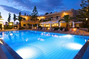 A swimming pool with lounge chairs and umbrellas, surrounded by a building with multiple balconies and outdoor seating areas. - Solimar Ruby (Hersonissos)