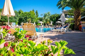 A pool area with lounge chairs and umbrellas, surrounded by greenery and a clear sky. - Solimar Ruby (Hersonissos)