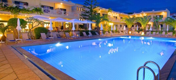 A swimming pool with lounge chairs and umbrellas, surrounded by a building with multiple balconies and outdoor seating areas. - Solimar Ruby (Hersonissos)