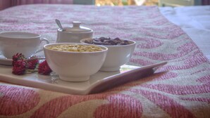 A bed with a tray of breakfast items, a view of a balcony with pink flowers, and a table with a hat. - Solimar Ruby (Hersonissos)