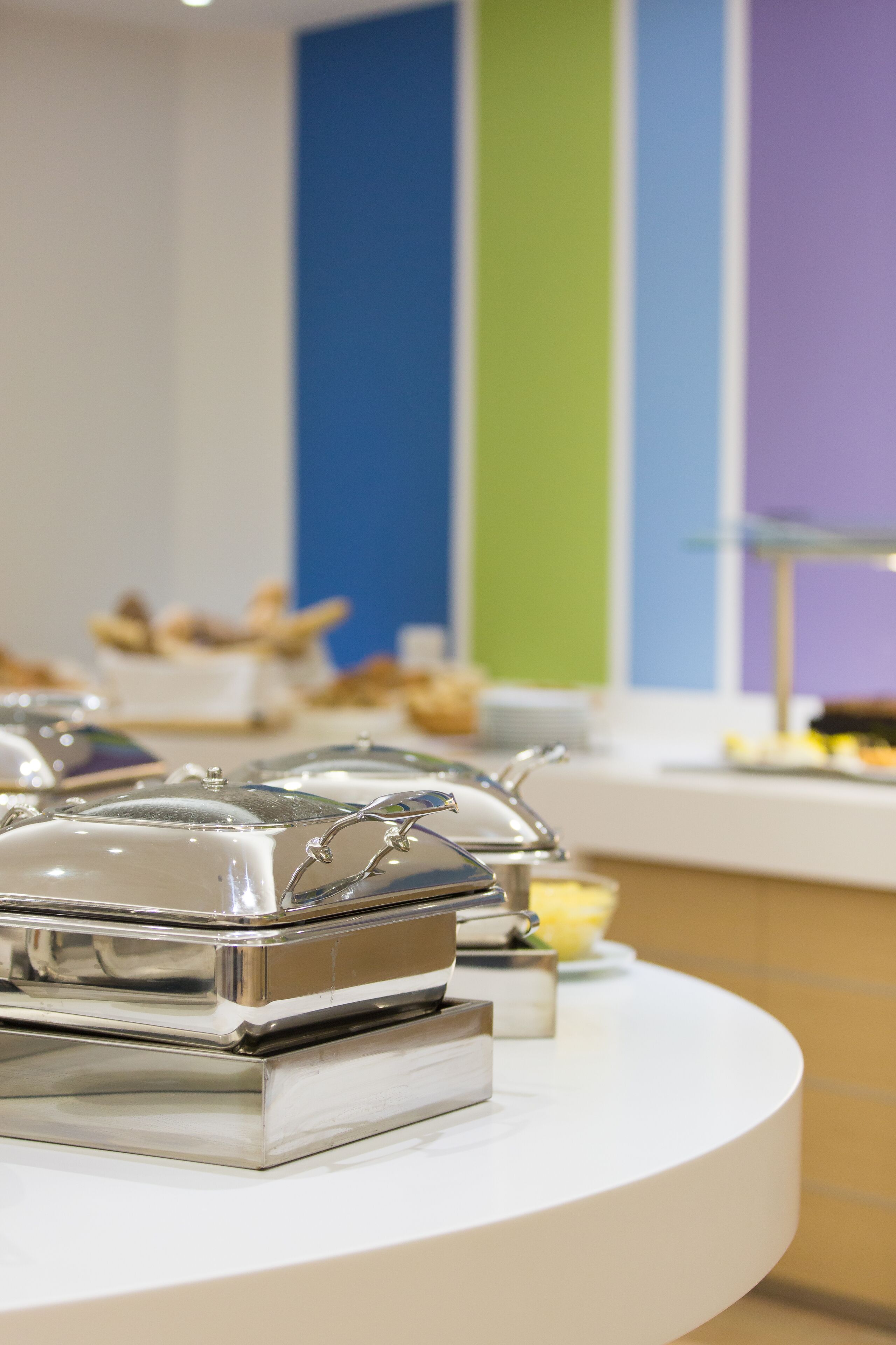 Ein reichhaltiges Buffet mit abgedeckten Speisebehältern auf einer weißen Tischplatte.
