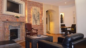 A living room with a fireplace, a television mounted above it, and a dining area with a table and chairs. - Citadella Residence Appartments Vienna (Vienna)