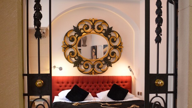 A bedroom with a red upholstered headboard, a large ornate mirror, and a bed with black bedding. - Citadella Residence Appartments Vienna (Vienna)
