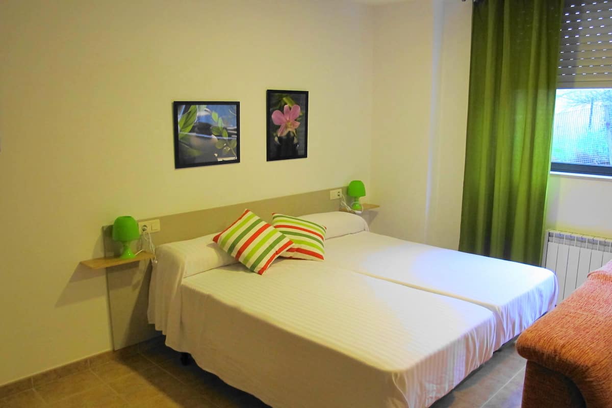A bedroom with a bed, pillows, a nightstand, a lamp, and two framed pictures on the wall.