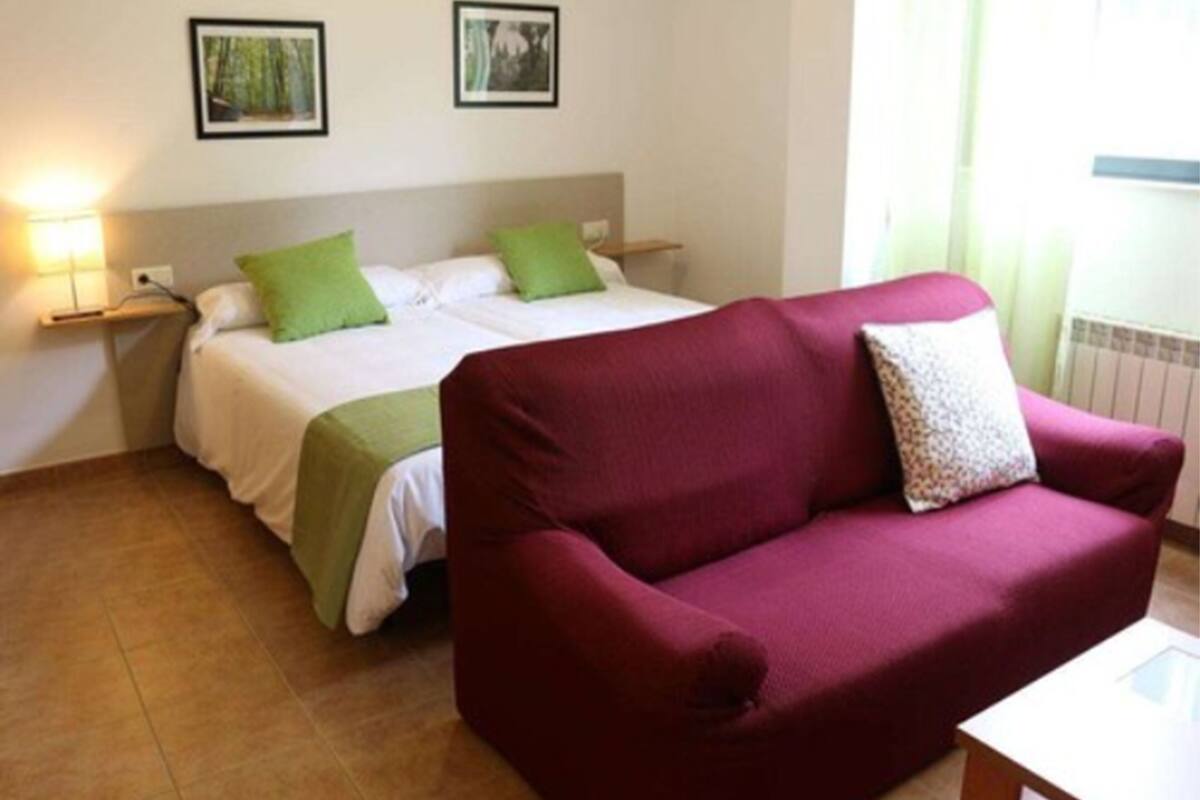 A hotel room with a bed, a red sofa, and two bedside tables with lamps.