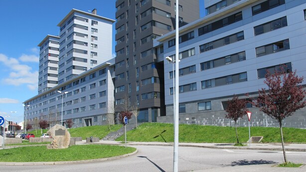 A modern urban setting with multi-story buildings, a pedestrian pathway, and a roundabout.