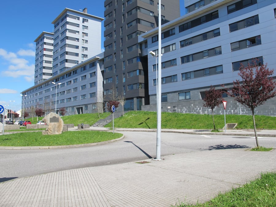 A modern urban setting with multi-story buildings, a pedestrian pathway, and a roundabout.