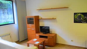 A compact room with a sofa, a wooden cabinet with drawers, a TV on a wooden stand, and a small table.