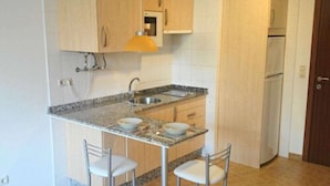 A compact kitchen with a granite countertop, two white bar stools, a built-in oven, and a refrigerator.