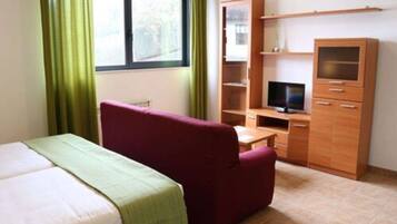 Een slaapkamer met een bed, een rode bank, een televisie en een houten kast.