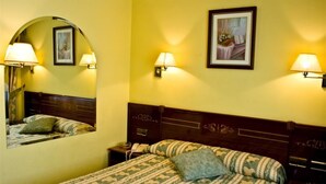 A hotel room with a bed, two bedside lamps, a nightstand with a phone, a mirror, and a framed picture on the wall.