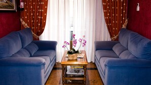 A room with two blue sofas facing each other, a wooden coffee table with a plant and books, and a red wall with a framed picture.