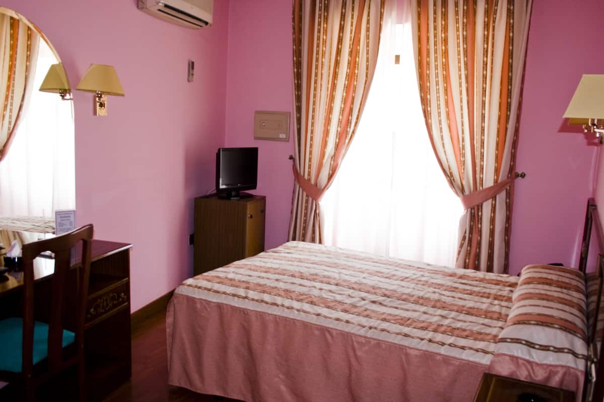 A room with a bed, a desk, a television, and curtains.