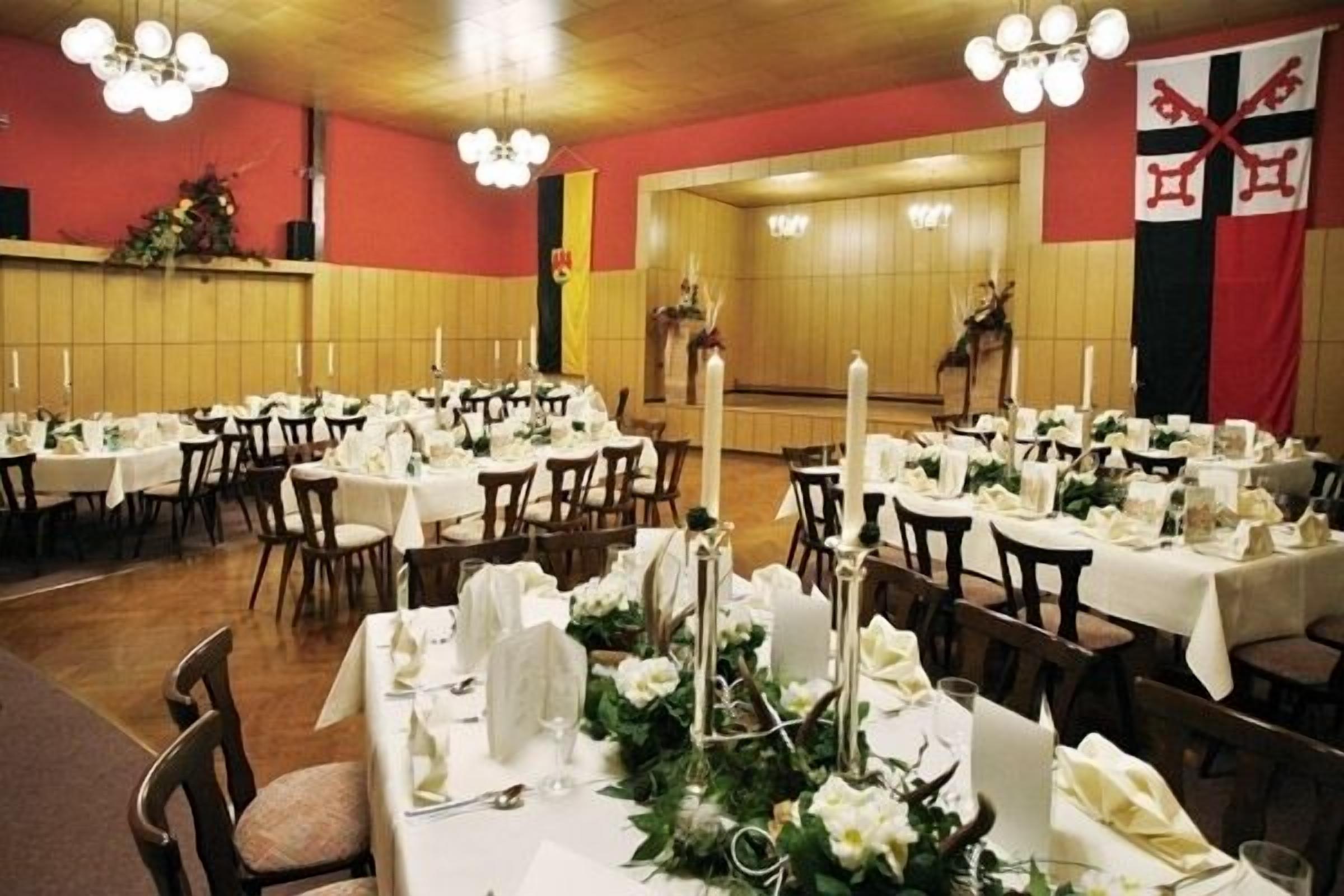 A banquet hall with multiple round tables set for dining, featuring white tablecloths and floral centerpieces.