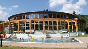 A modern building with a pool area, featuring a large glass facade, outdoor seating, and a slide. - Gasthaus Kupfer (Südharz)