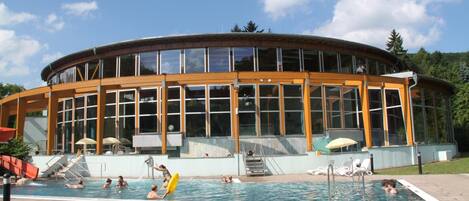 A modern building with a pool area, featuring a large glass facade, outdoor seating, and a slide.