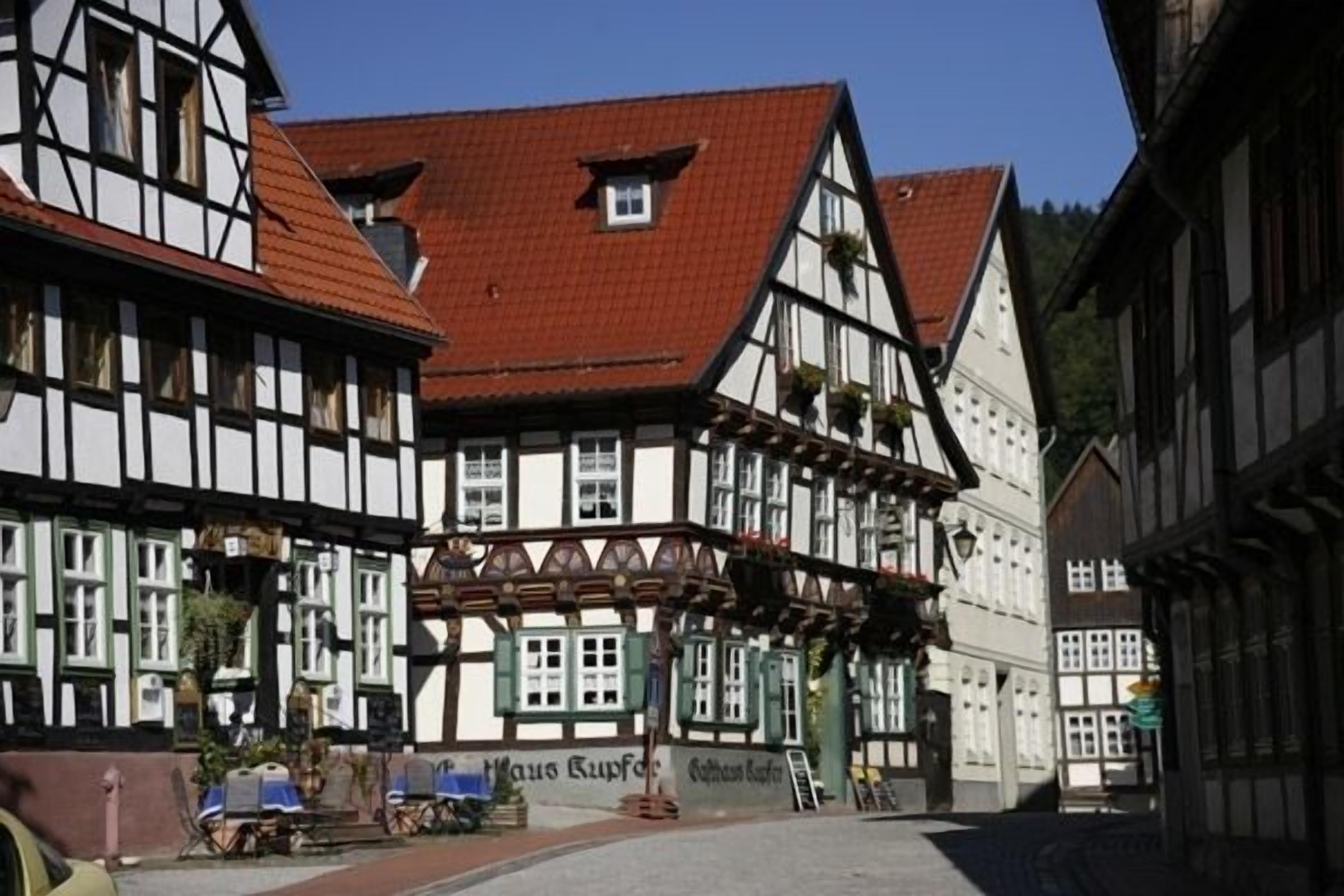 A traditional half-timbered building with a red-tiled roof, a sign reading "Haus Kupfer," and a small outdoor seating area with tables and chairs.
