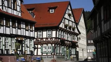 A traditional half-timbered building with a red-tiled roof, a sign reading "Haus Kupfer," and a small outdoor seating area with tables and chairs.