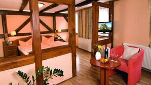 A cozy room with a bed, a red sofa, a table with fruit and a bottle, and a TV. - Gasthaus Kupfer (Südharz)