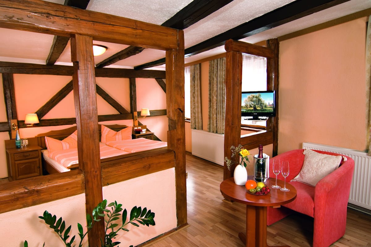 A cozy room with a bed, a red sofa, a table with fruit and a bottle, and a TV.