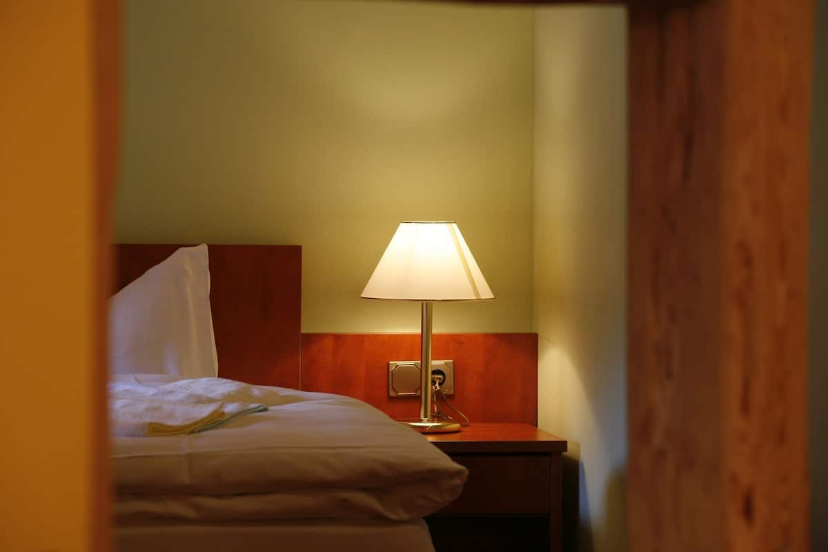 A hotel room with a bed, a nightstand, and a lamp.