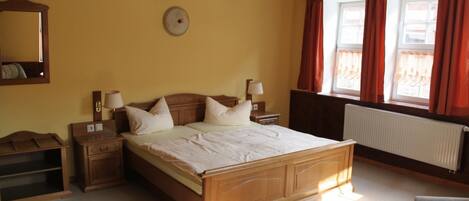 A bedroom with a wooden bed, two bedside tables, a nightstand, a mirror, and a window with curtains.