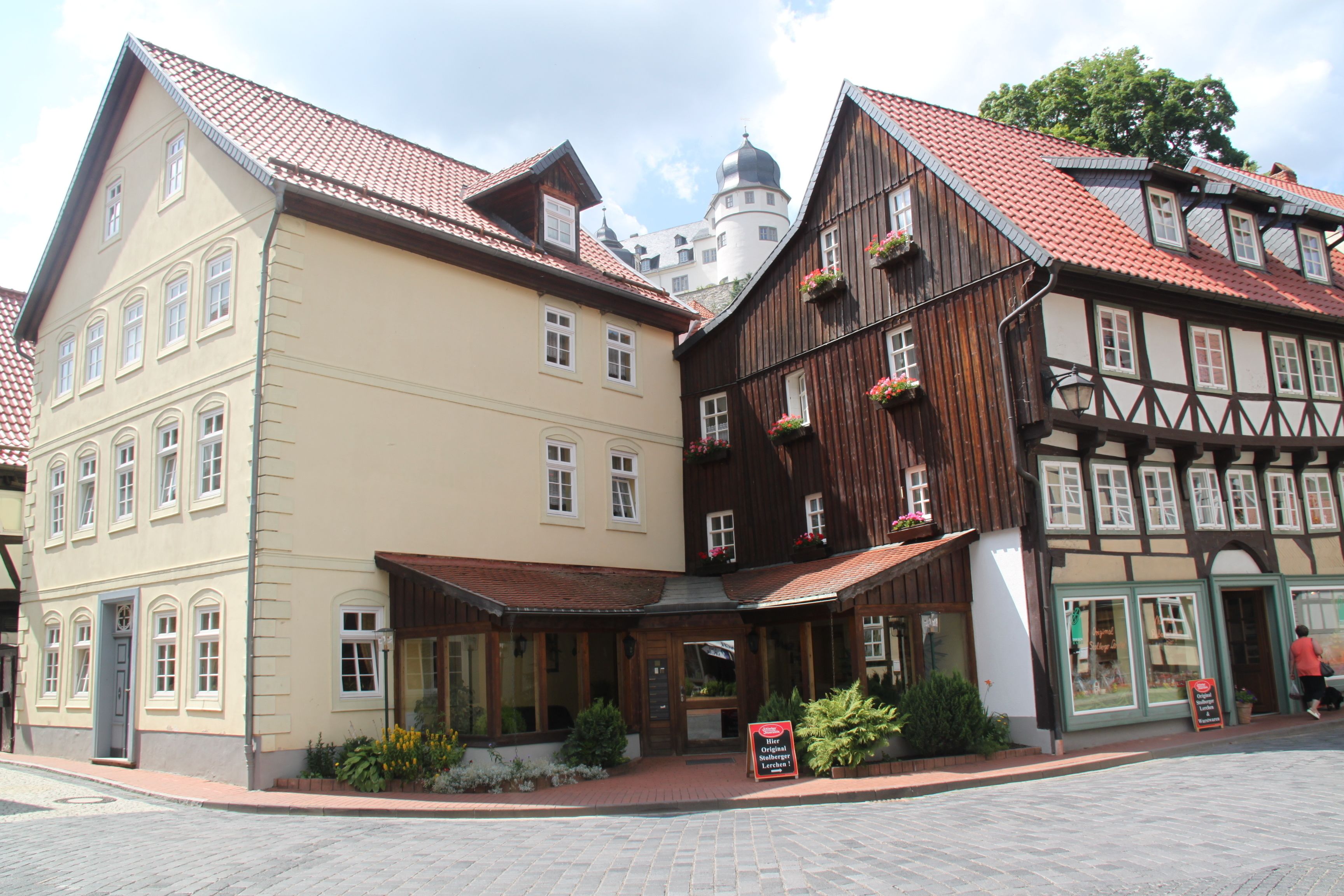 A traditional European building with a red-tiled roof, a balcony with flowers, and a signboard.