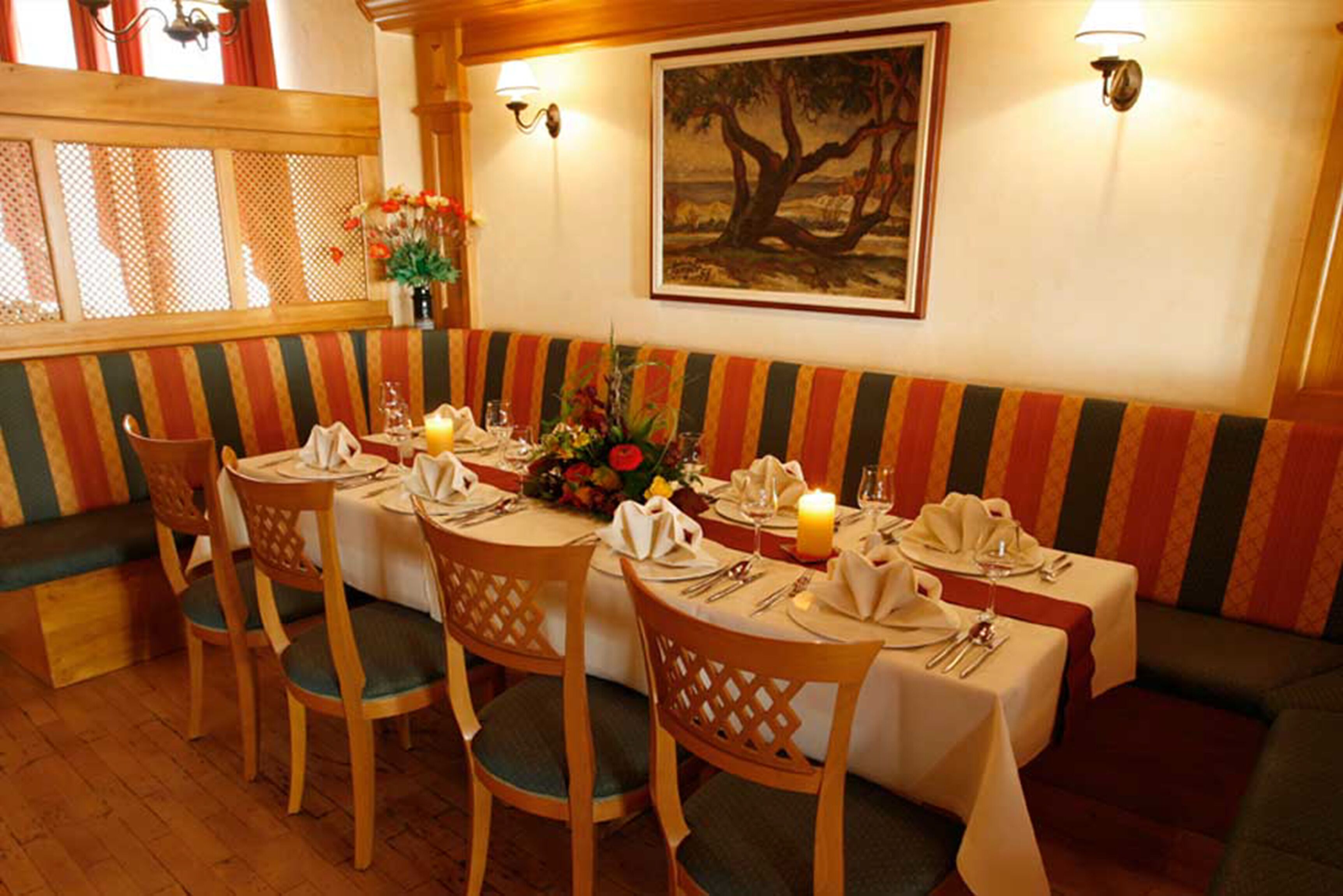 A restaurant with a long table set for four, wooden chairs, a bench, and a wall-mounted painting.