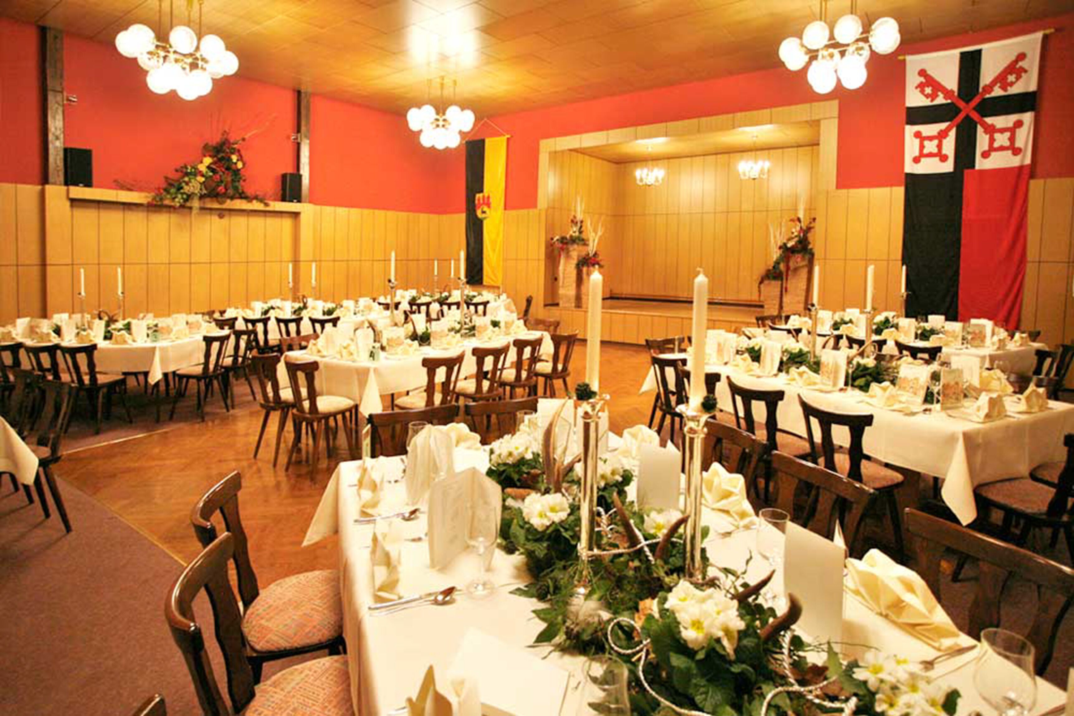A banquet hall with multiple round tables set for dining, featuring white tablecloths and candle centerpieces.