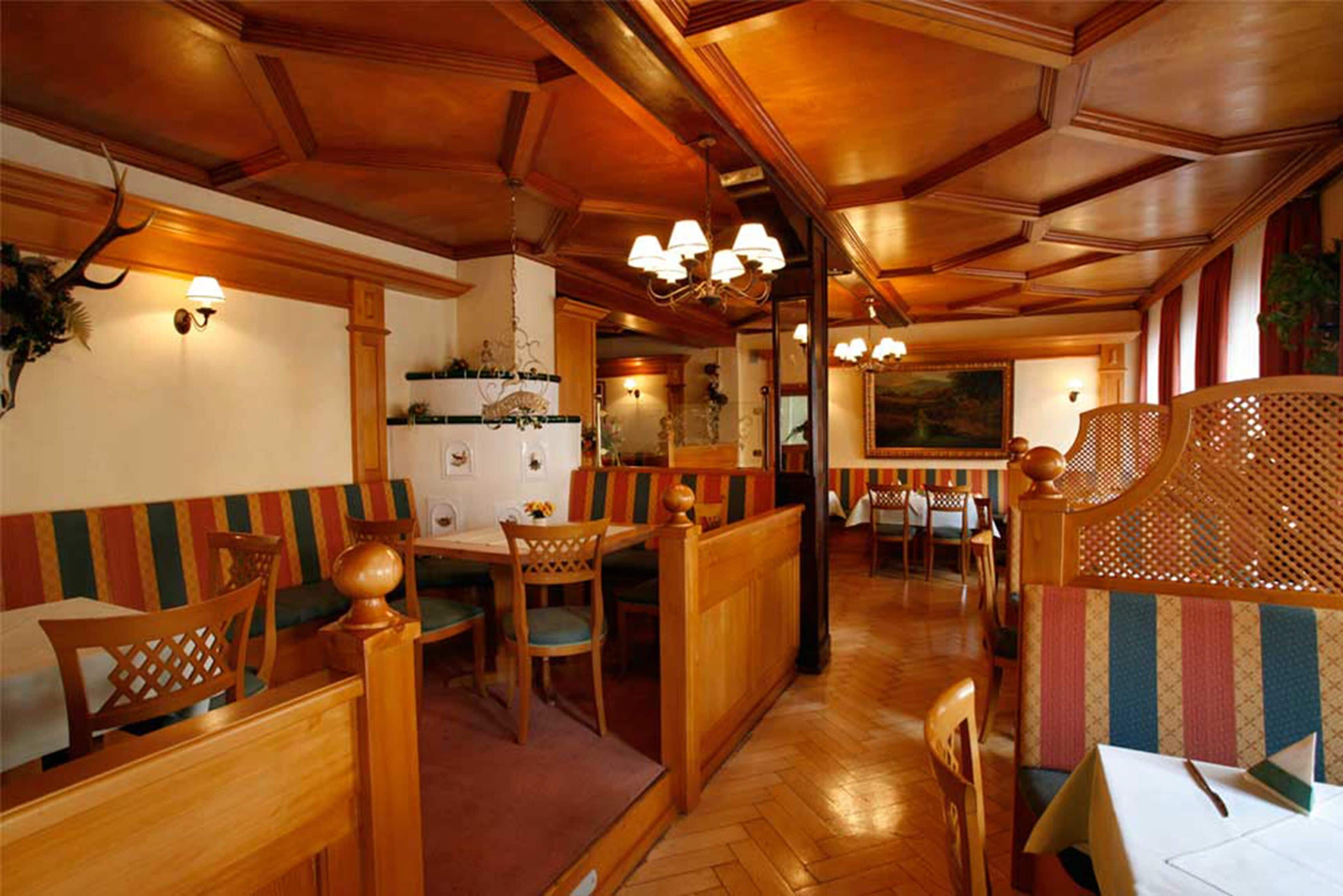 A wooden interior with booths and tables, wooden ceiling beams, and wall-mounted lamps.