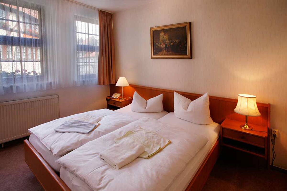 A hotel room with two beds, white linens, a painting on the wall, and two bedside lamps.