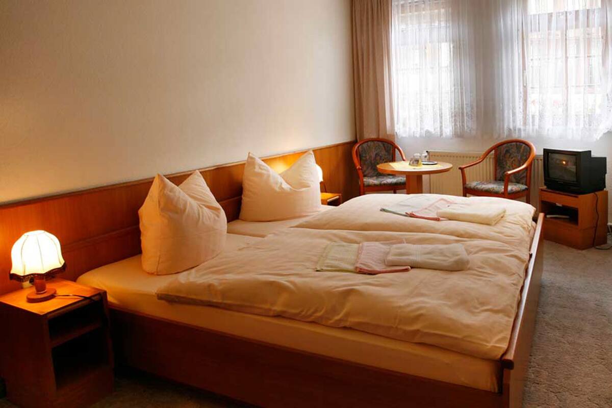 A hotel room with a large bed, two bedside tables, a lamp, a TV, and two chairs.