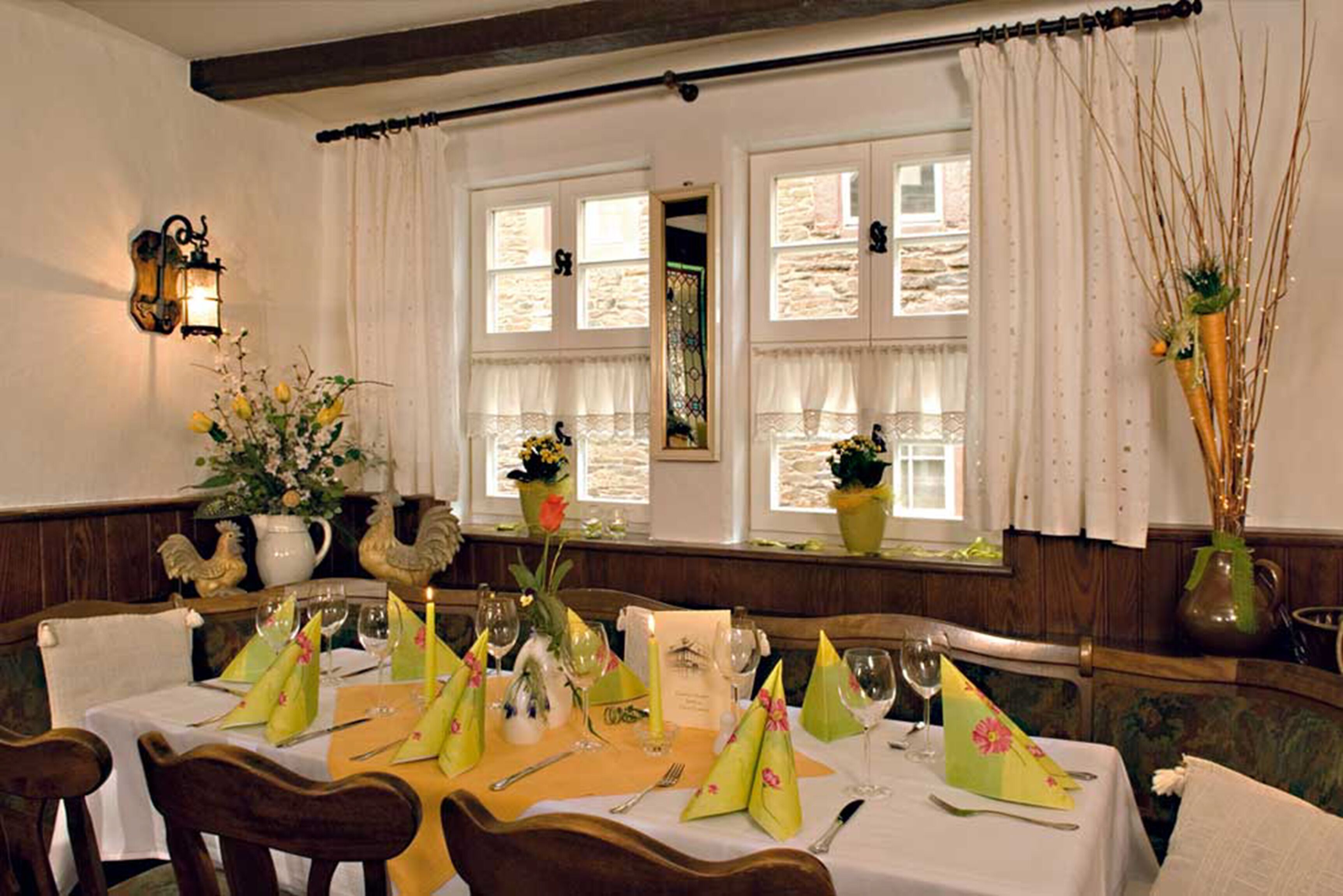 A dining area with a table set for four, featuring yellow napkins, a candle, and a vase with flowers.