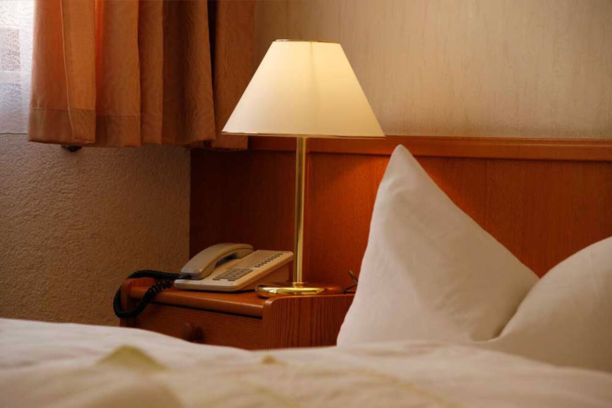 A hotel room with a bed, a bedside lamp, a telephone, and a wooden headboard.