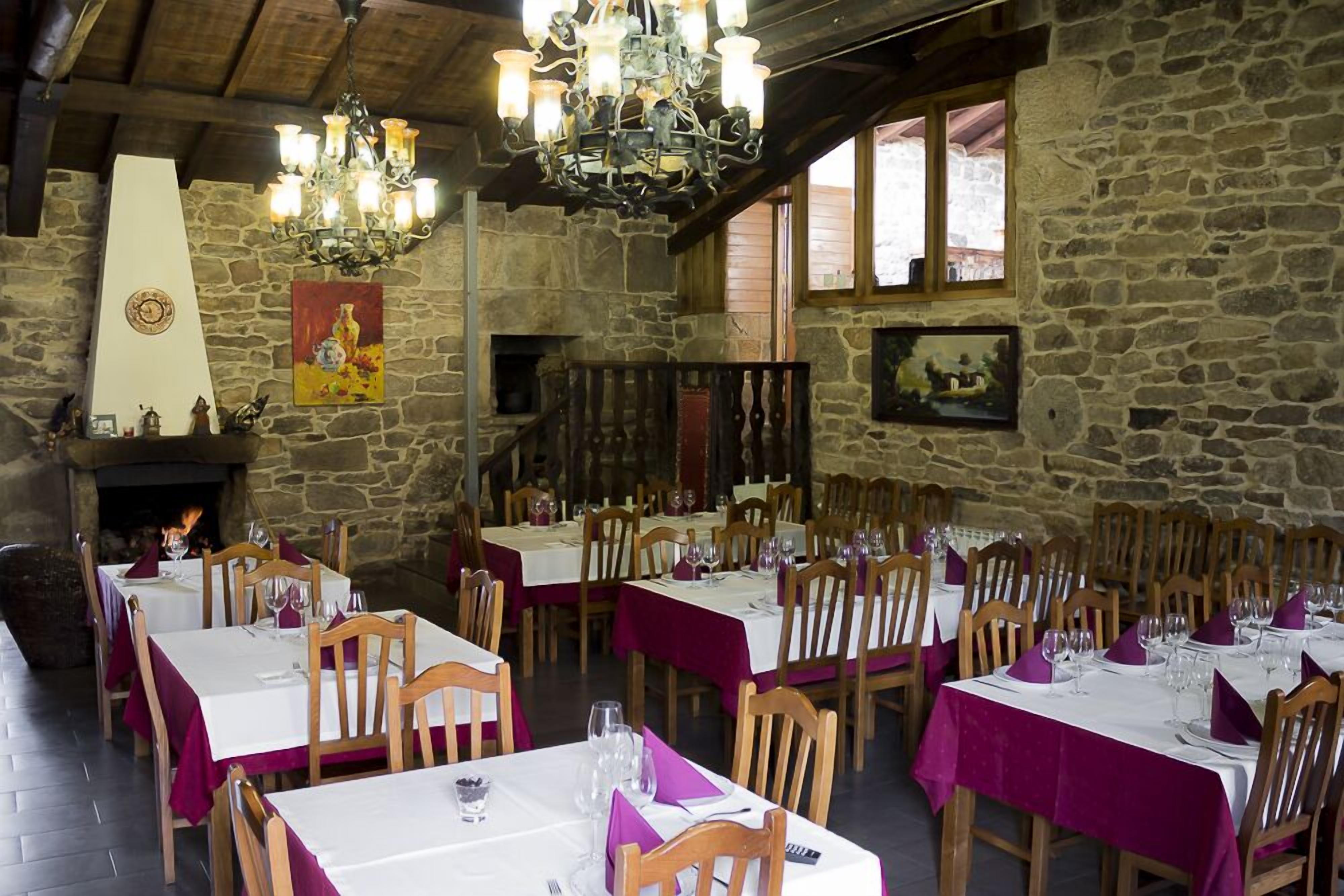 A rustic dining area with stone walls, wooden tables, and a chandelier.