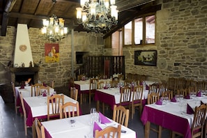 Un comedor rústico con paredes de piedra, mesas de madera y un candelabro.
