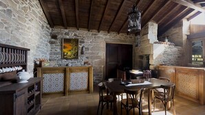 Una cocina rústica con paredes de piedra, vigas de madera, una mesa de comedor con sillas y una zona de bar con mostrador de piedra.