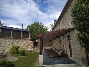 Un edificio de piedra con un patio cubierto que cuenta con sillones de madera y un sendero de piedra.