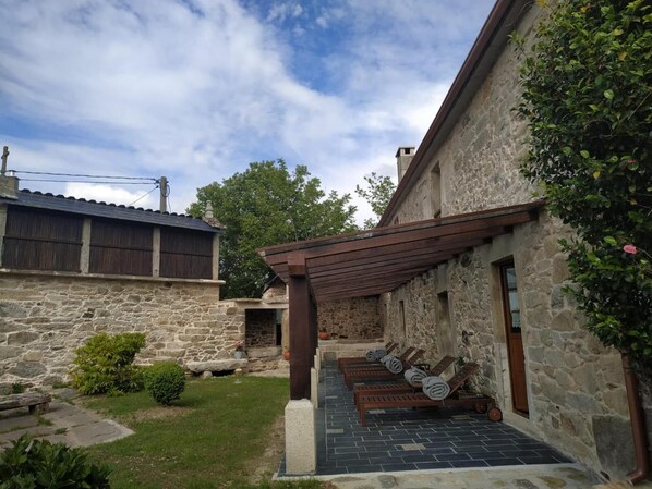 Un edificio de piedra con un patio cubierto que cuenta con sillones de madera y un sendero de piedra.