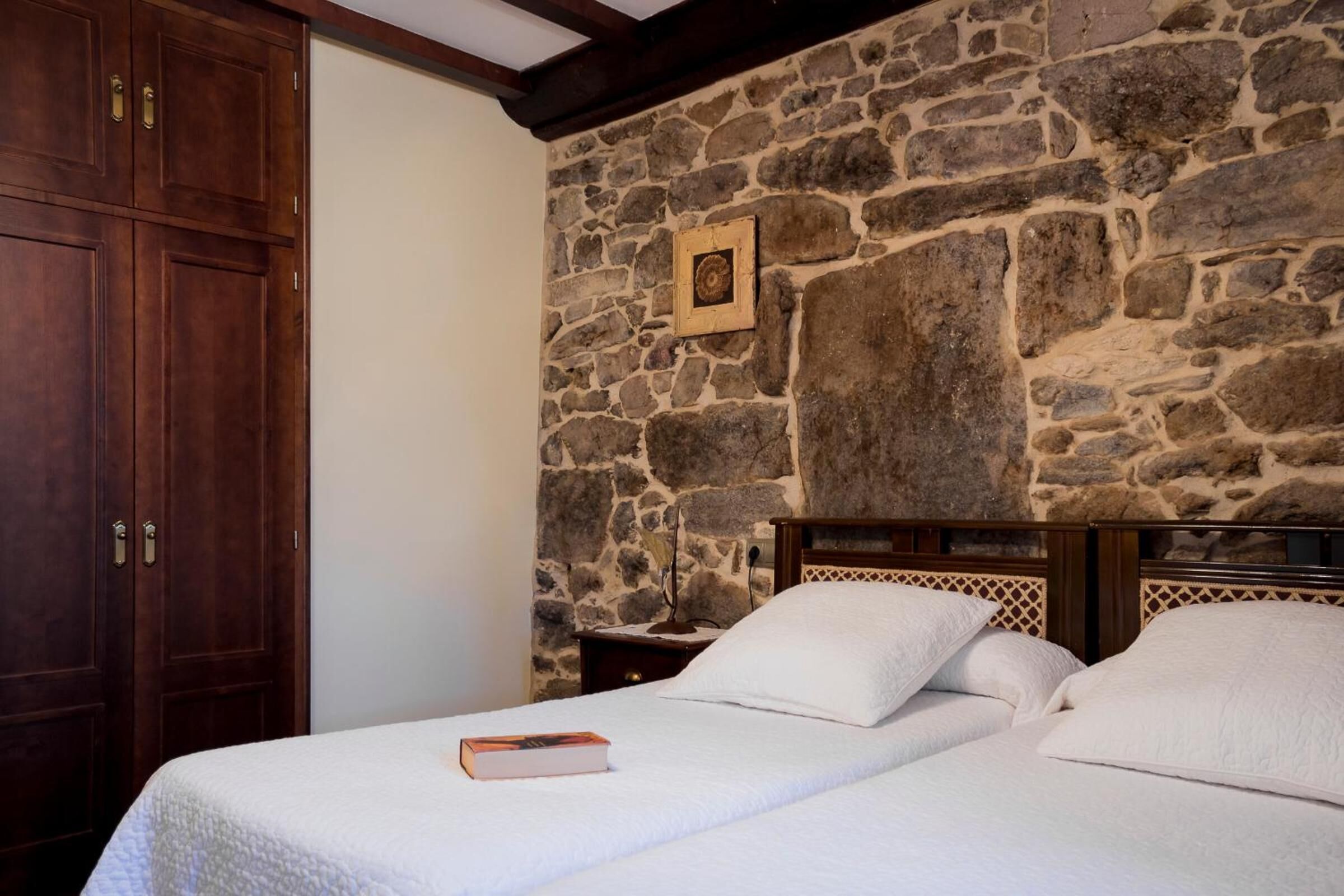 Una camera da letto con parete in pietra, armadio in legno e letto con biancheria bianca.
