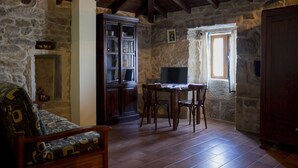 Una habitación rústica con paredes de piedra, techo de madera, chimenea, televisor y una mesa de comedor con sillas.
