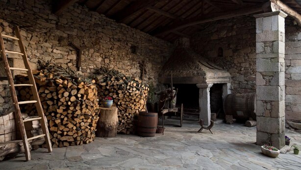 Un edificio rústico de piedra con techo de madera, pared de piedra y entrada con tejado de paja.