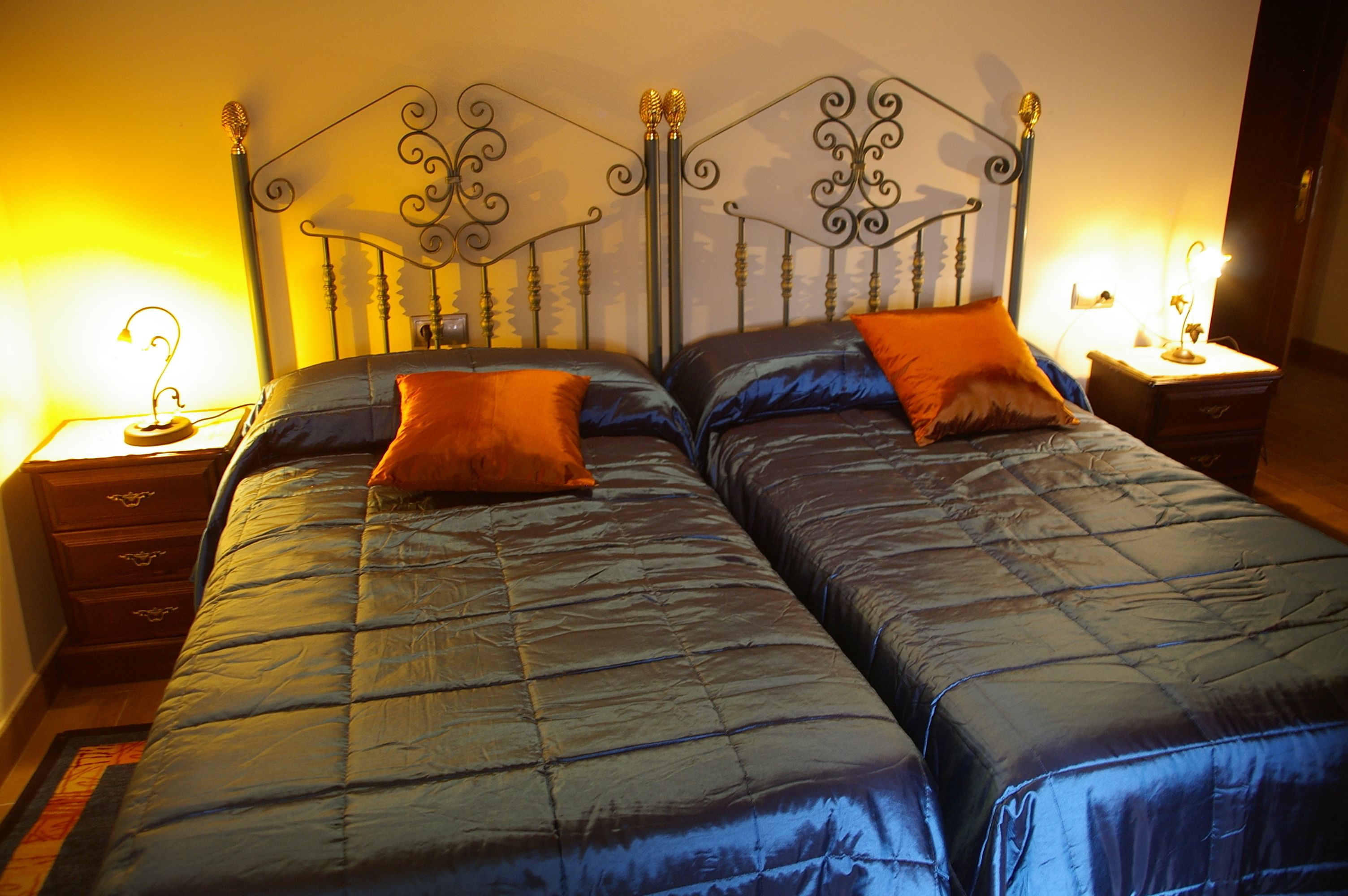 A double bed with a metal headboard, two bedside tables with lamps, and a blue quilted bedspread.